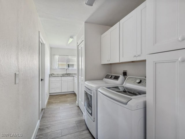 laundry area featuring washing machine and dryer, cabinet space, light wood finished floors, and a sink