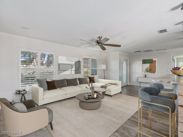 living room with visible vents, baseboards, ceiling fan, ornamental molding, and wood finished floors