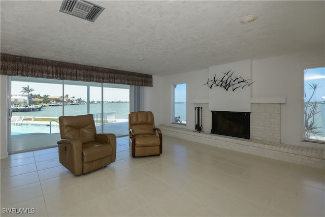 living room featuring a textured ceiling, light tile patterned floors, a water view, a fireplace, and visible vents