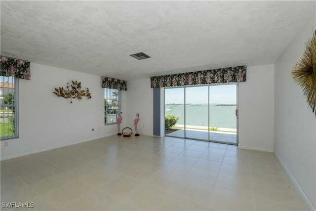 empty room with visible vents, a water view, a textured ceiling, and baseboards