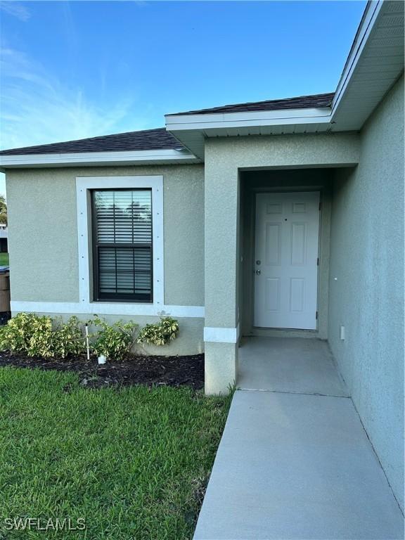 doorway to property with roof with shingles and stucco siding