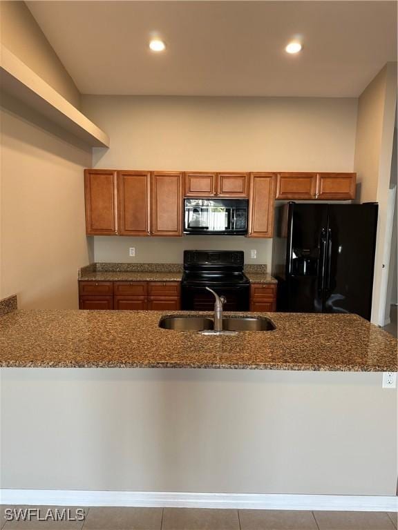 kitchen featuring black appliances, dark stone countertops, brown cabinets, and a sink