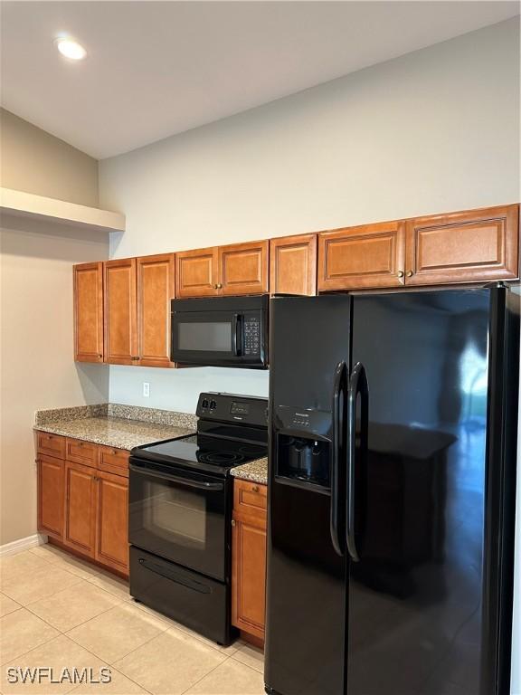 kitchen featuring light stone counters, black appliances, and brown cabinetry