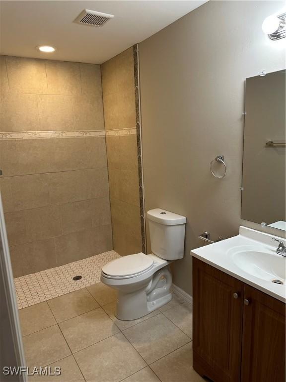 bathroom with vanity, visible vents, a tile shower, tile patterned flooring, and toilet