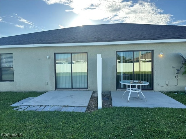 rear view of property featuring a yard, a patio area, roof with shingles, and stucco siding