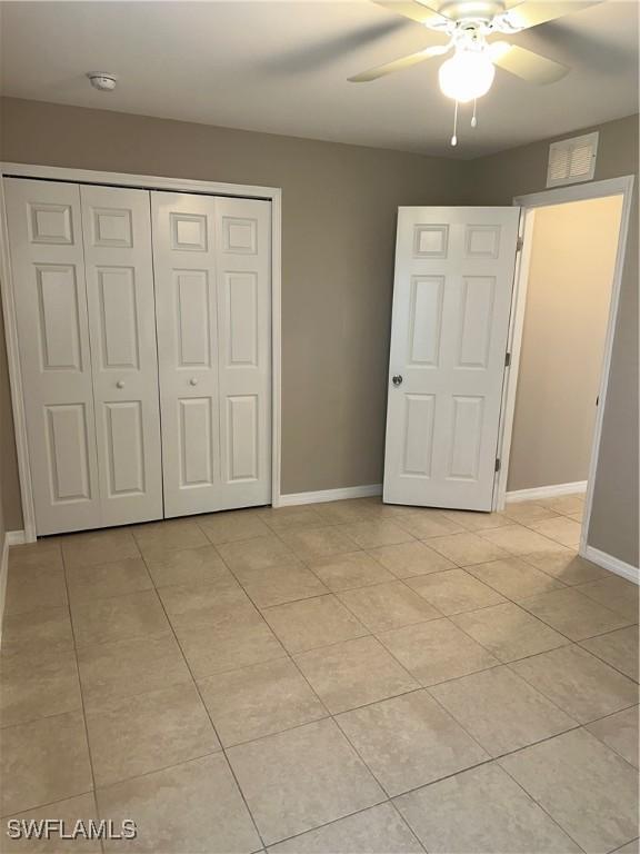 unfurnished bedroom with light tile patterned floors, a closet, baseboards, and a ceiling fan