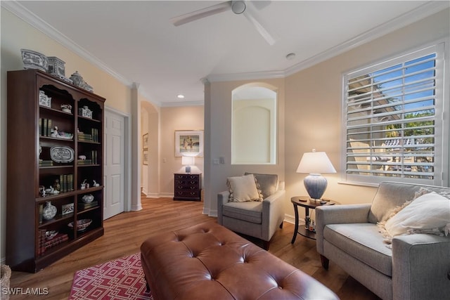 living room featuring arched walkways, wood finished floors, a ceiling fan, baseboards, and ornamental molding