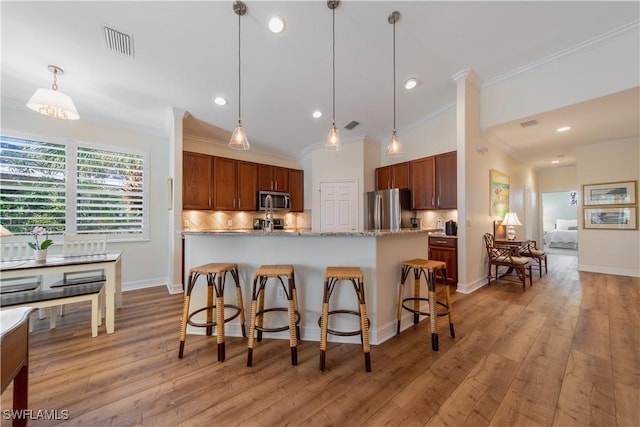 kitchen with hanging light fixtures, appliances with stainless steel finishes, backsplash, and light wood-style flooring