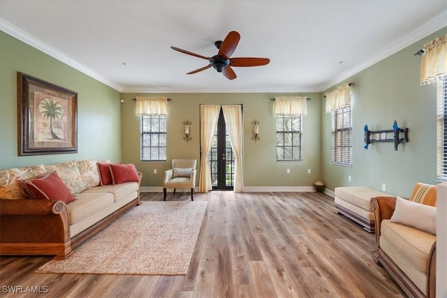 living area featuring light wood-style flooring, ornamental molding, ceiling fan, and baseboards