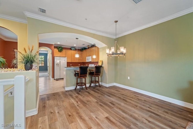 kitchen with light wood-style flooring, white appliances, visible vents, a kitchen breakfast bar, and decorative light fixtures