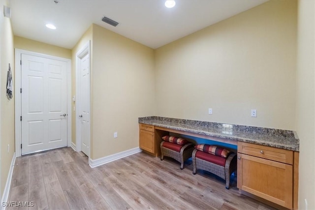 interior space with light wood-type flooring, built in study area, visible vents, and baseboards