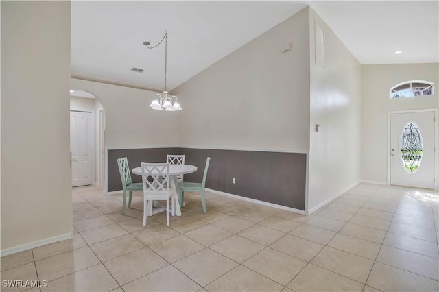 unfurnished dining area with arched walkways, high vaulted ceiling, a chandelier, and tile patterned floors