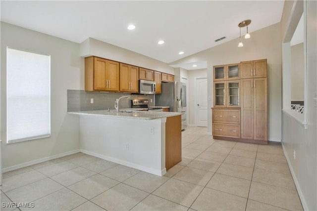 kitchen featuring lofted ceiling, a peninsula, appliances with stainless steel finishes, brown cabinets, and tasteful backsplash