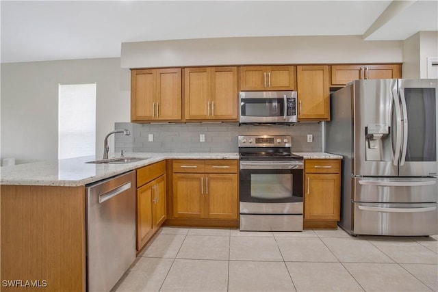 kitchen with tasteful backsplash, brown cabinets, light stone countertops, stainless steel appliances, and a sink