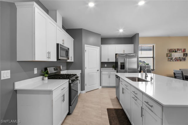 kitchen featuring light countertops, appliances with stainless steel finishes, white cabinetry, a sink, and an island with sink