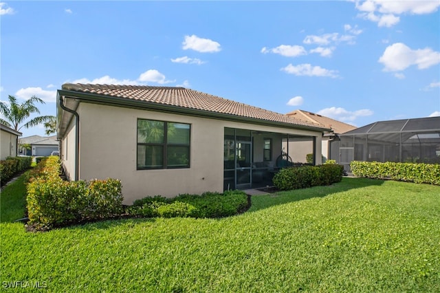 rear view of house with a tiled roof, a lawn, a sunroom, and stucco siding