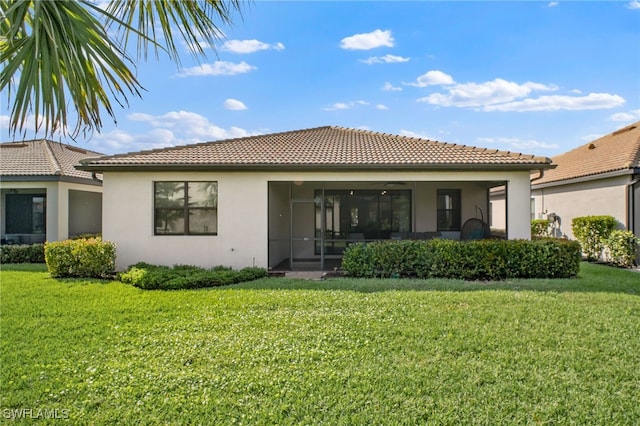 rear view of house with a sunroom, a tile roof, a yard, and stucco siding