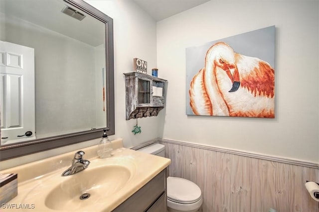 bathroom featuring visible vents, wainscoting, toilet, vanity, and wood walls