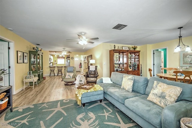 living area featuring light wood-style flooring, visible vents, ceiling fan, and baseboards