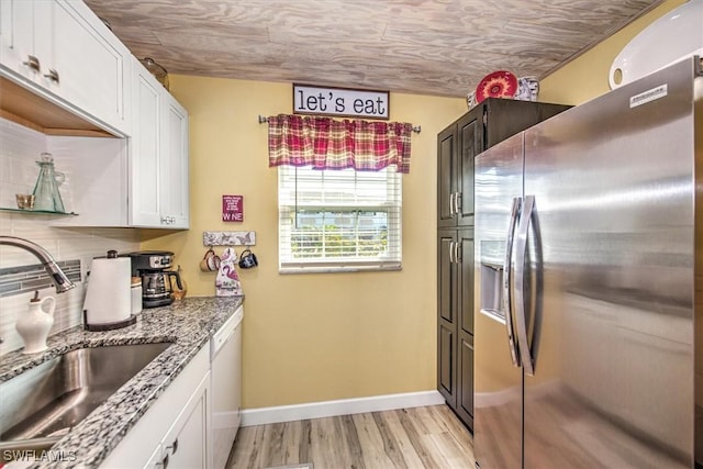 kitchen featuring stainless steel fridge, white cabinets, dishwasher, a sink, and backsplash