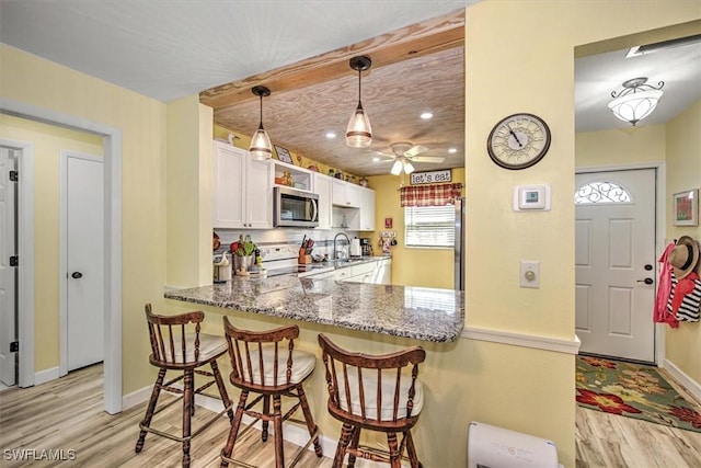 kitchen with white electric stove, stainless steel microwave, decorative light fixtures, a peninsula, and white cabinetry