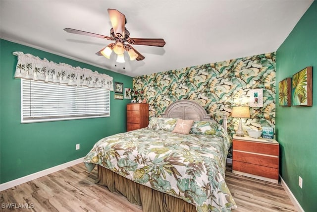 bedroom featuring an accent wall, wood finished floors, baseboards, and wallpapered walls