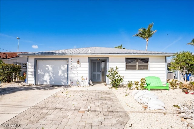 single story home with an attached garage, metal roof, and concrete driveway