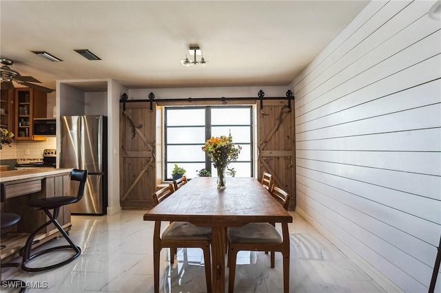 16221 Buccaneer St, Bokeelia, FL 33922 - dining area with marble finish floor, visible vents, a barn door, and wood walls