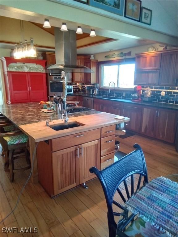 kitchen with cooktop, a sink, island range hood, wood finished floors, and oven