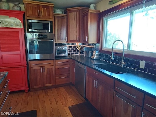 kitchen with decorative backsplash, appliances with stainless steel finishes, brown cabinets, light wood-style floors, and a sink