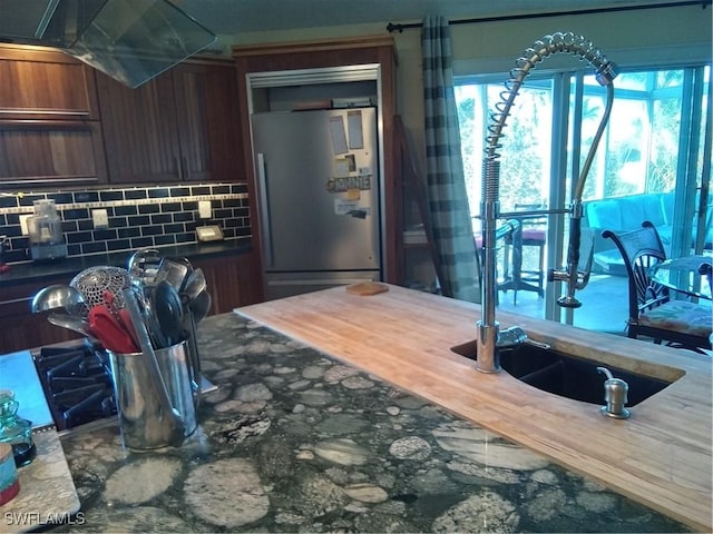 kitchen with tasteful backsplash, dark countertops, exhaust hood, and freestanding refrigerator