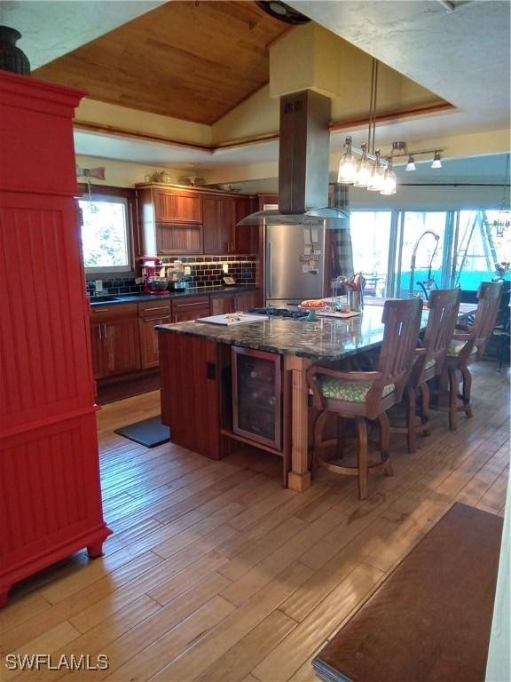 kitchen with a tray ceiling, backsplash, light wood-style flooring, and island range hood