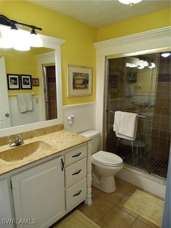 bathroom featuring a wainscoted wall, toilet, a shower stall, vanity, and tile patterned flooring