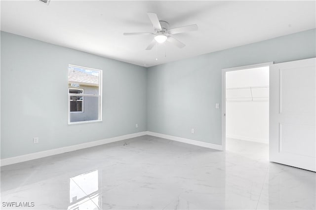 spare room with ceiling fan, marble finish floor, and baseboards