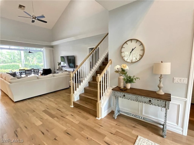 living room featuring visible vents, a ceiling fan, wood finished floors, high vaulted ceiling, and stairs