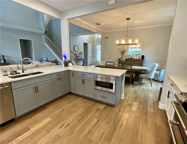 kitchen featuring light countertops, hanging light fixtures, appliances with stainless steel finishes, a sink, and a peninsula