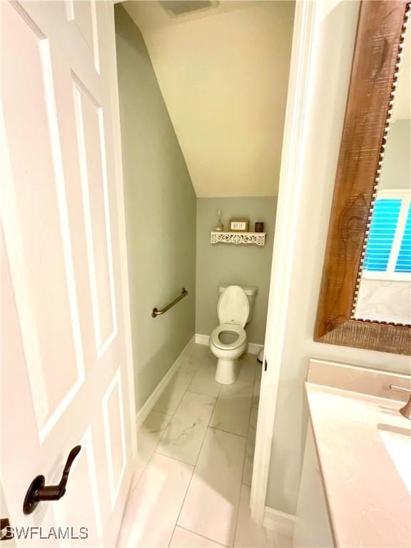 bathroom featuring lofted ceiling, marble finish floor, toilet, and baseboards