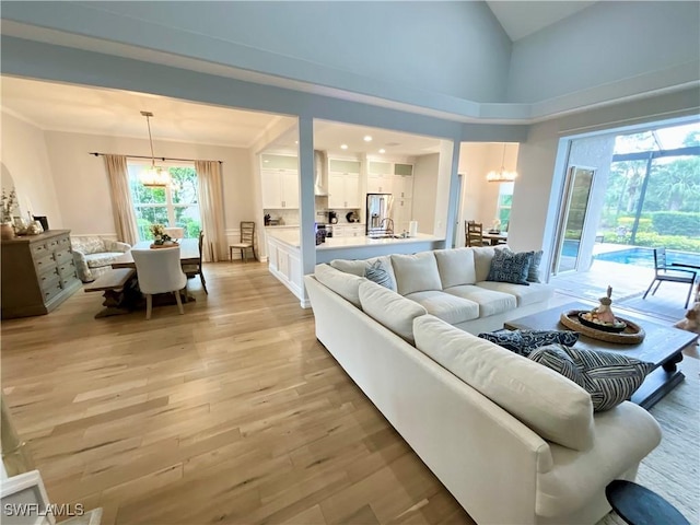 living room with light wood-style floors, crown molding, a towering ceiling, and an inviting chandelier