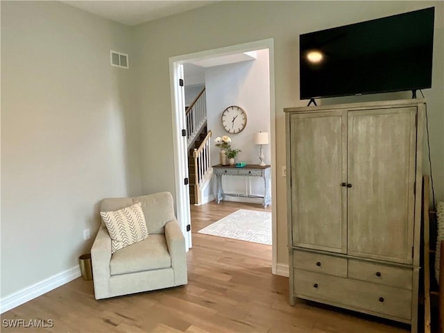 sitting room with light wood-type flooring, stairway, baseboards, and visible vents