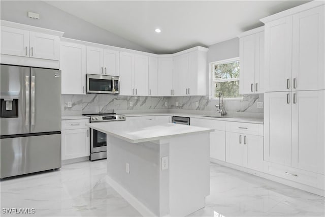 kitchen with a sink, vaulted ceiling, marble finish floor, appliances with stainless steel finishes, and light countertops