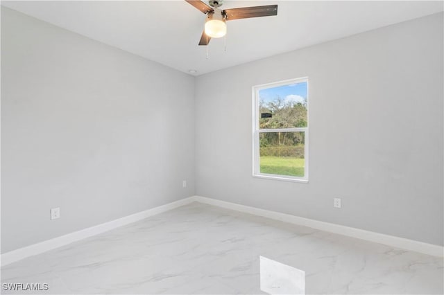 spare room featuring a ceiling fan, marble finish floor, and baseboards