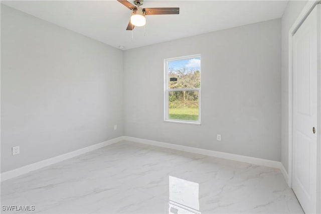 unfurnished room with ceiling fan, marble finish floor, and baseboards