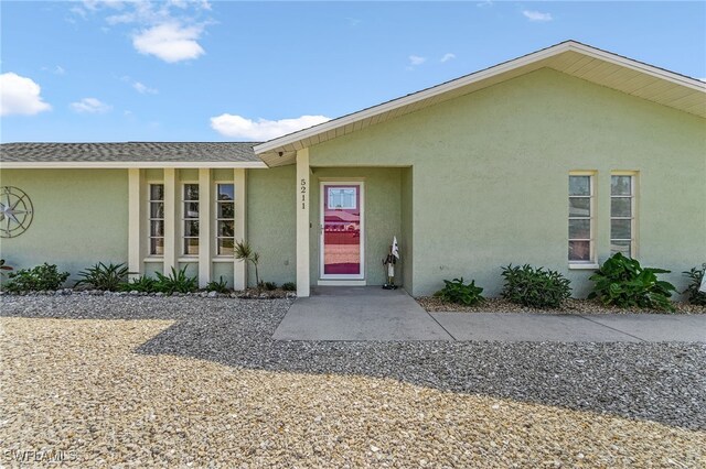 doorway to property featuring a shingled roof and stucco siding