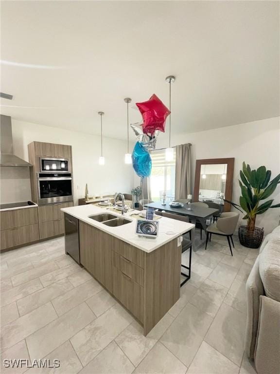 kitchen with a sink, wall chimney range hood, black appliances, an island with sink, and modern cabinets