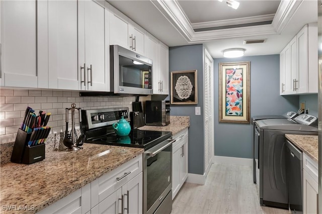 kitchen featuring visible vents, appliances with stainless steel finishes, ornamental molding, washing machine and clothes dryer, and a tray ceiling