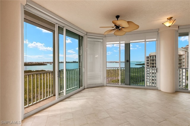 unfurnished sunroom with a ceiling fan and a water view