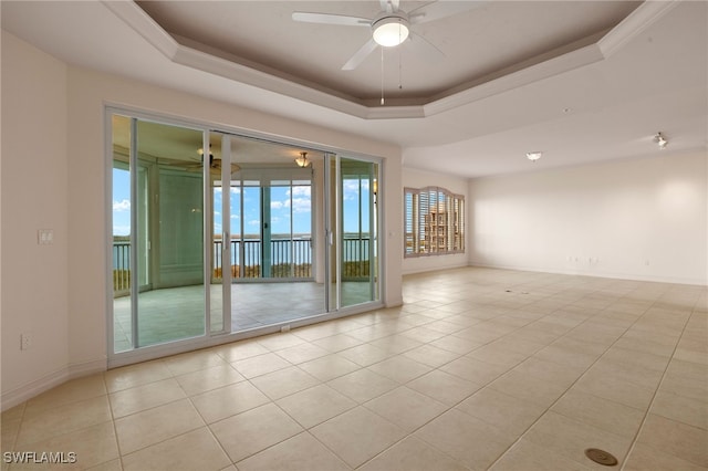 tiled empty room with ceiling fan, a tray ceiling, and a healthy amount of sunlight