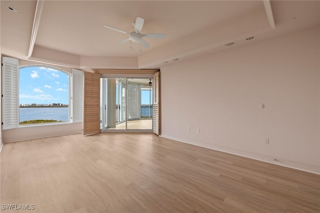 empty room featuring a water view, light wood finished floors, baseboards, and a ceiling fan