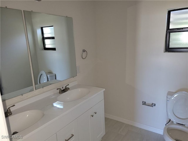 full bath featuring toilet, double vanity, baseboards, and a sink