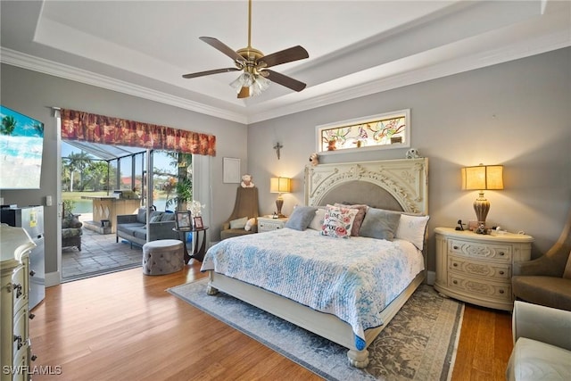 bedroom featuring access to exterior, crown molding, a raised ceiling, and wood finished floors